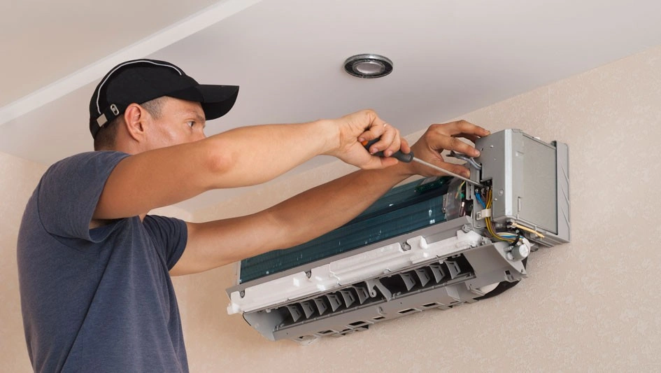Mini Split AC In Trinity, TX 1 Technician in Black Cap & T-shirt repairing an AC Unit.