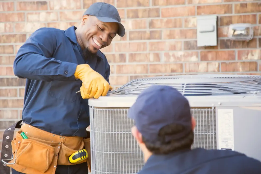 Emergency Air Conditioner Repair In Shepherd, TX 1 HVAC technicians in blue uniforms servicing outdoor AC unit near brick wall