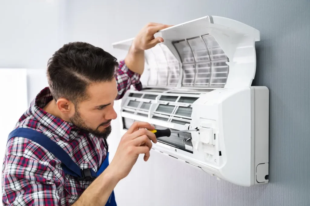 HVAC in Coldspring, TX 1 Technician in plaid shirt repairing wall-mounted air conditioner with screwdriver