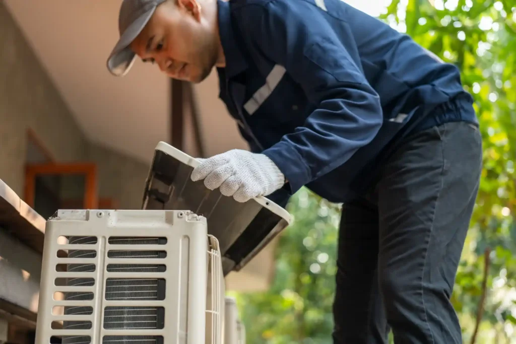 Air Conditioner Installation In Livingston, TX 1 Technician in blue uniform inspecting outdoor air conditioner with lifted cover
