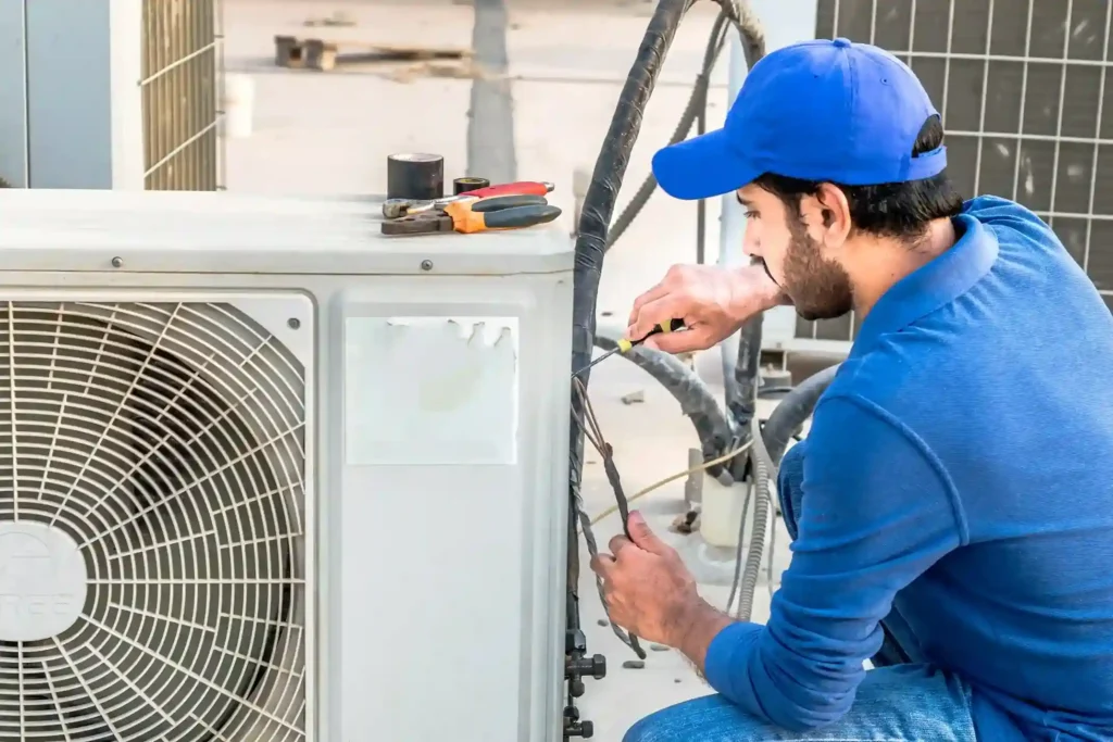 Heat Pump Installation In Coldspring, TX 1 Technician in blue shirt repairing AC unit wiring with tools on top